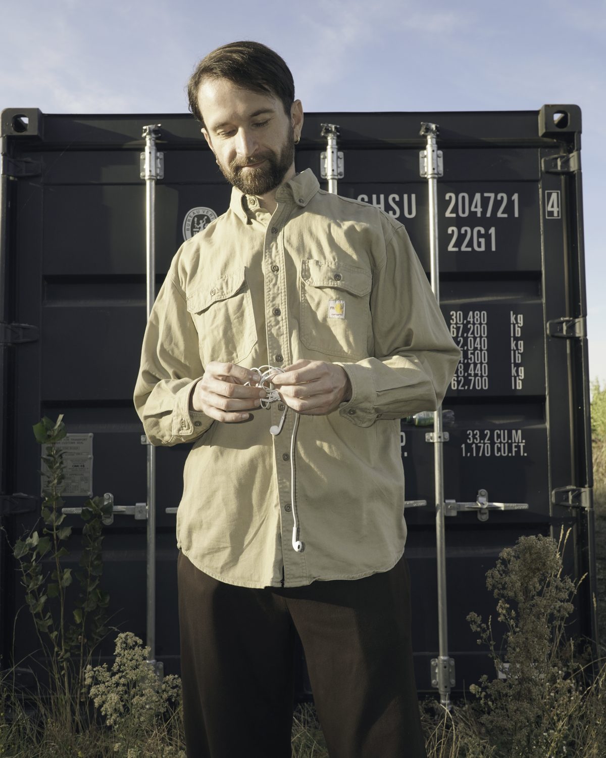 Tobias untangling a pair of wired earphones in front of a shipping container