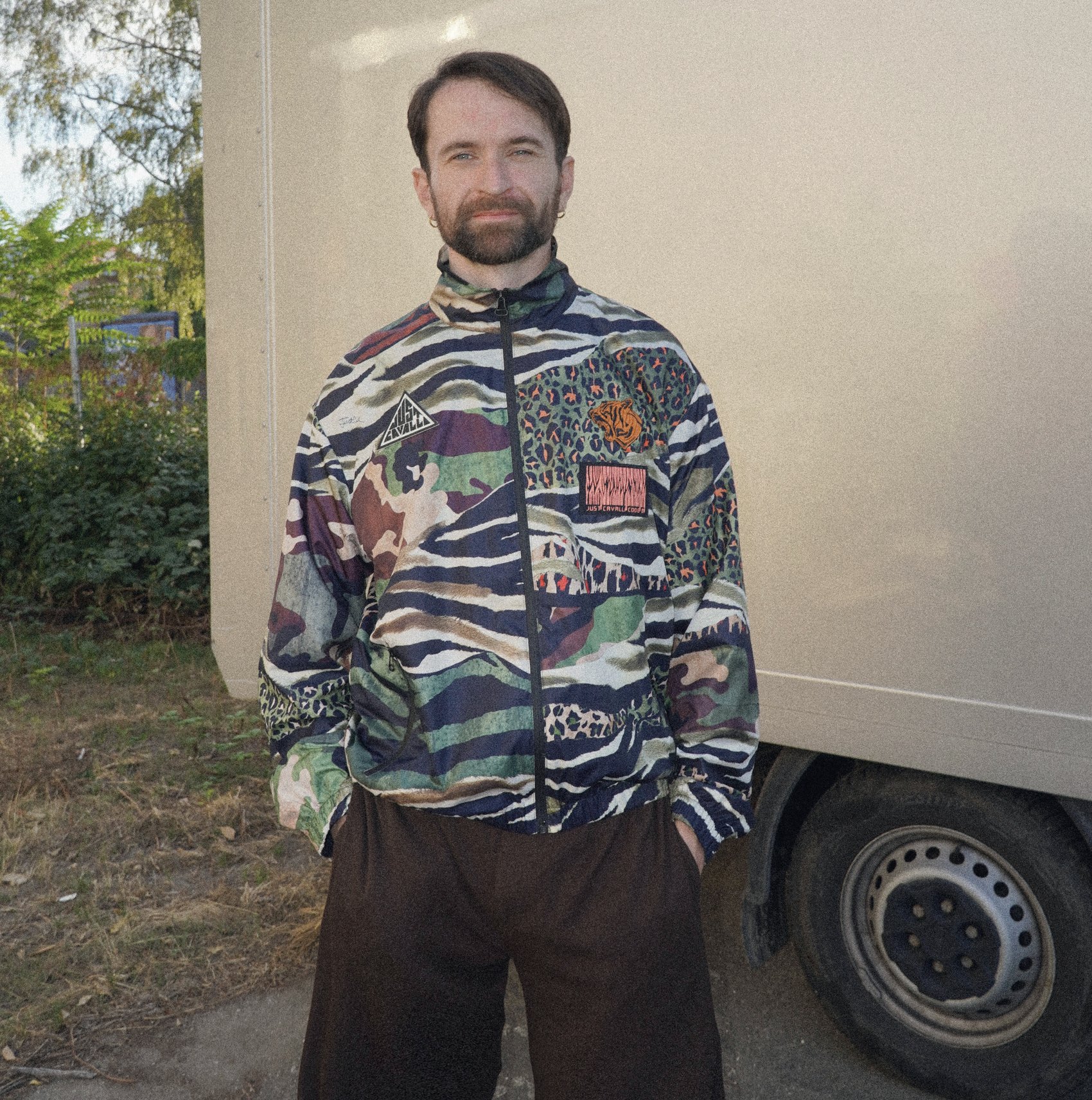 Tobias smiling in a patterned track jacket in front of a white van