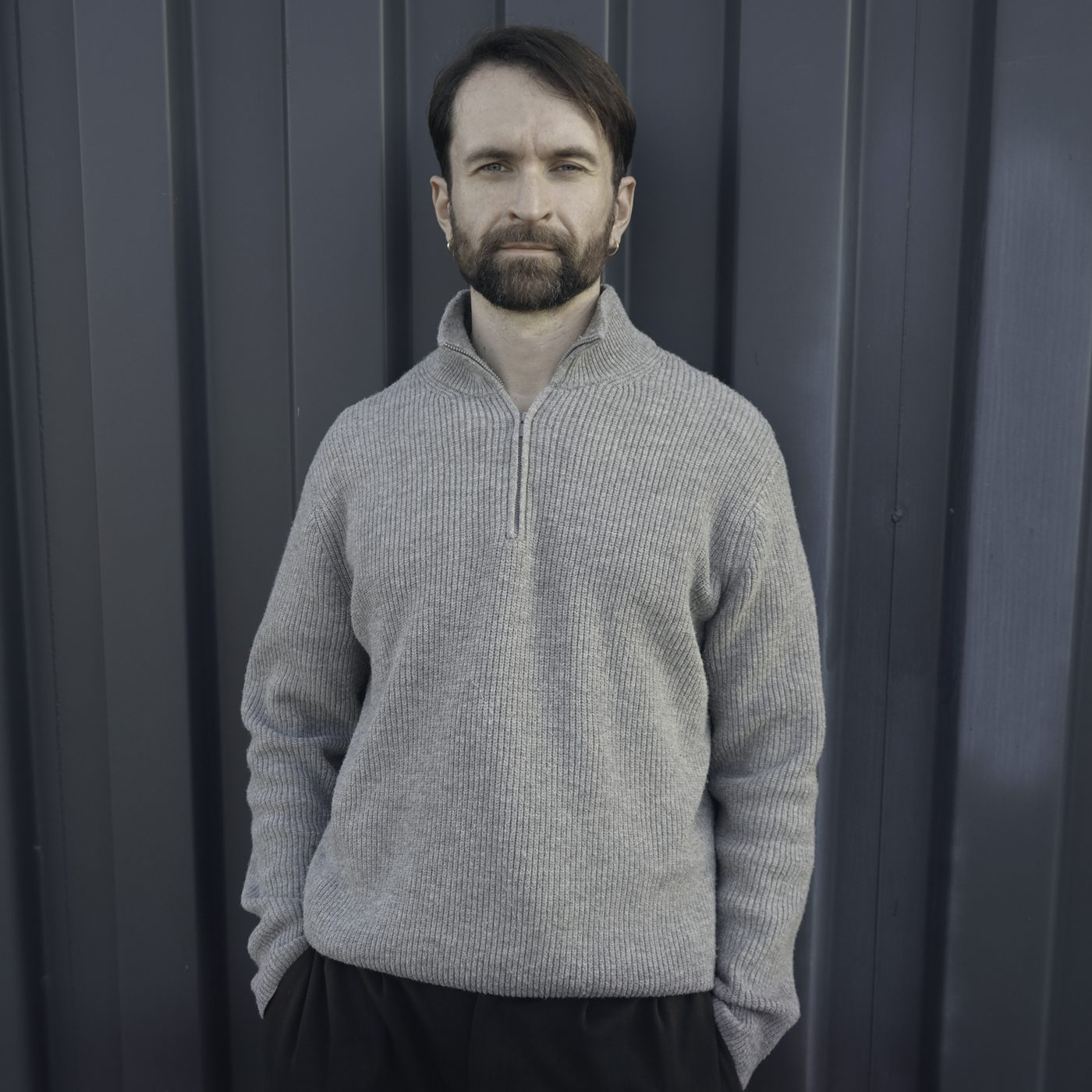Tobias Metzger in a grey knit sweater in front of a blue-grey corrugated wall